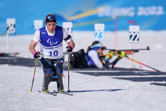A female sit-skier is in action, skiing in front of a shooting range